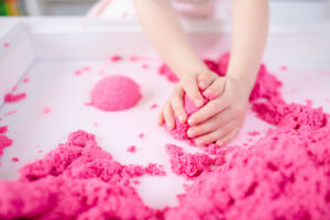 pink magic sand in kid's hands on a white background close up
