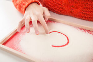 child writing letter "C" on sand, close up